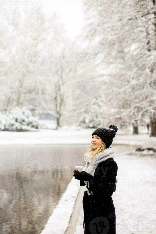 Young woman in warm clothes enjoying in snow with takeaway coffee cup photo