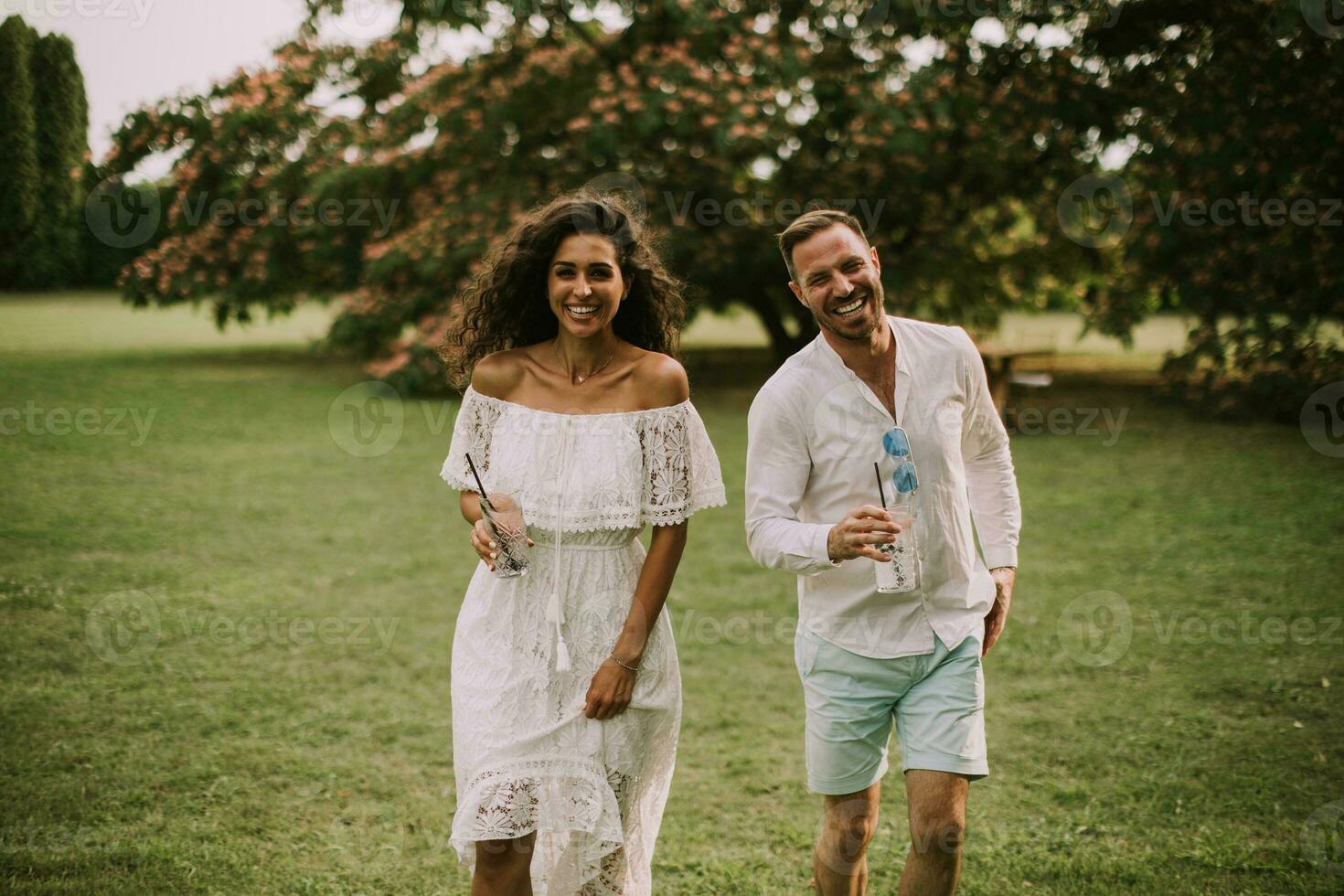 A happy young couple is enjoying the beautiful surroundings of a garden with glasses of fresh lemonade photo