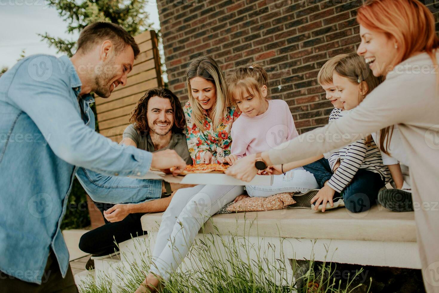 Group of young people and kids eating pizza in the house backyard photo