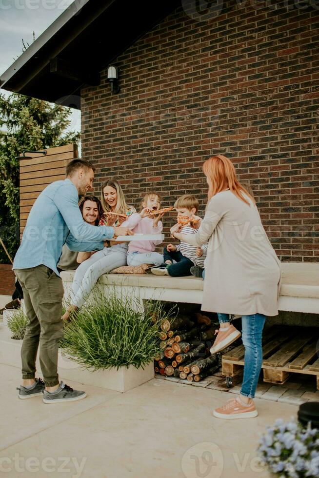 Group of young people and kids eating pizza in the house backyard photo