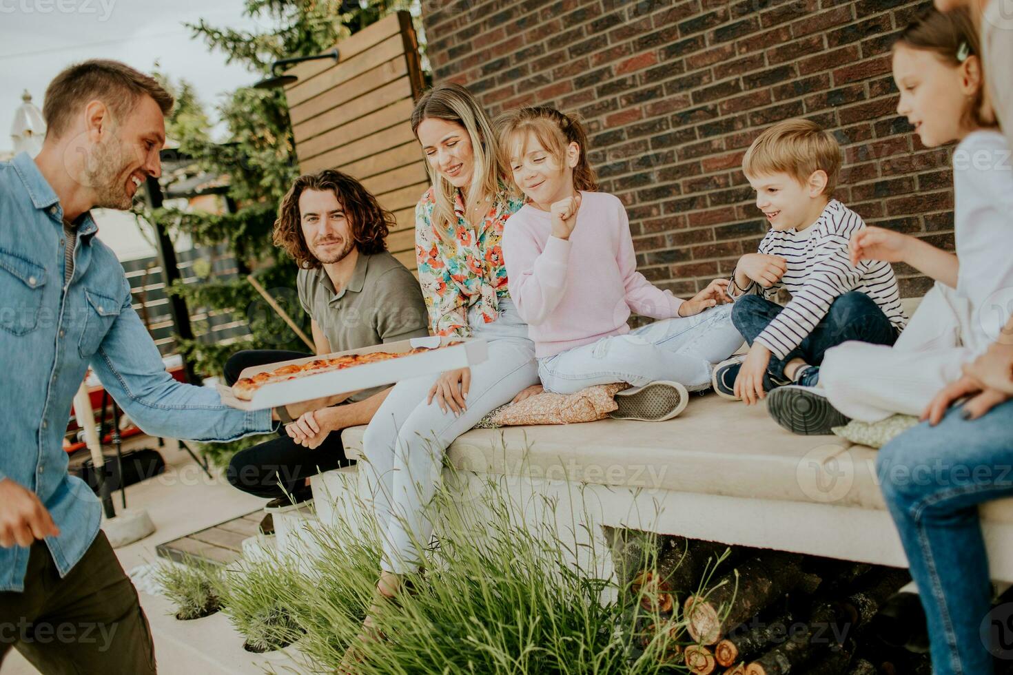 Group of young people and kids eating pizza in the house backyard photo