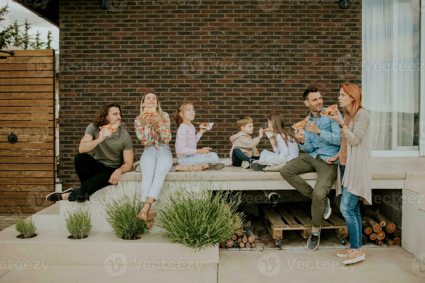 Group of young people and kids eating pizza in the house backyard photo