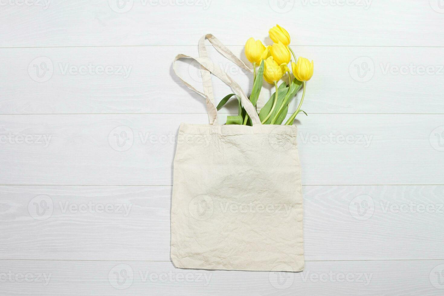 Mockup shopper handbag. Yellow tulips. Wood background. Top view copy space shopping eco reusable bag. Mothers women day. Template blank top view white cotton material canvas cloth. Empty mock-up photo