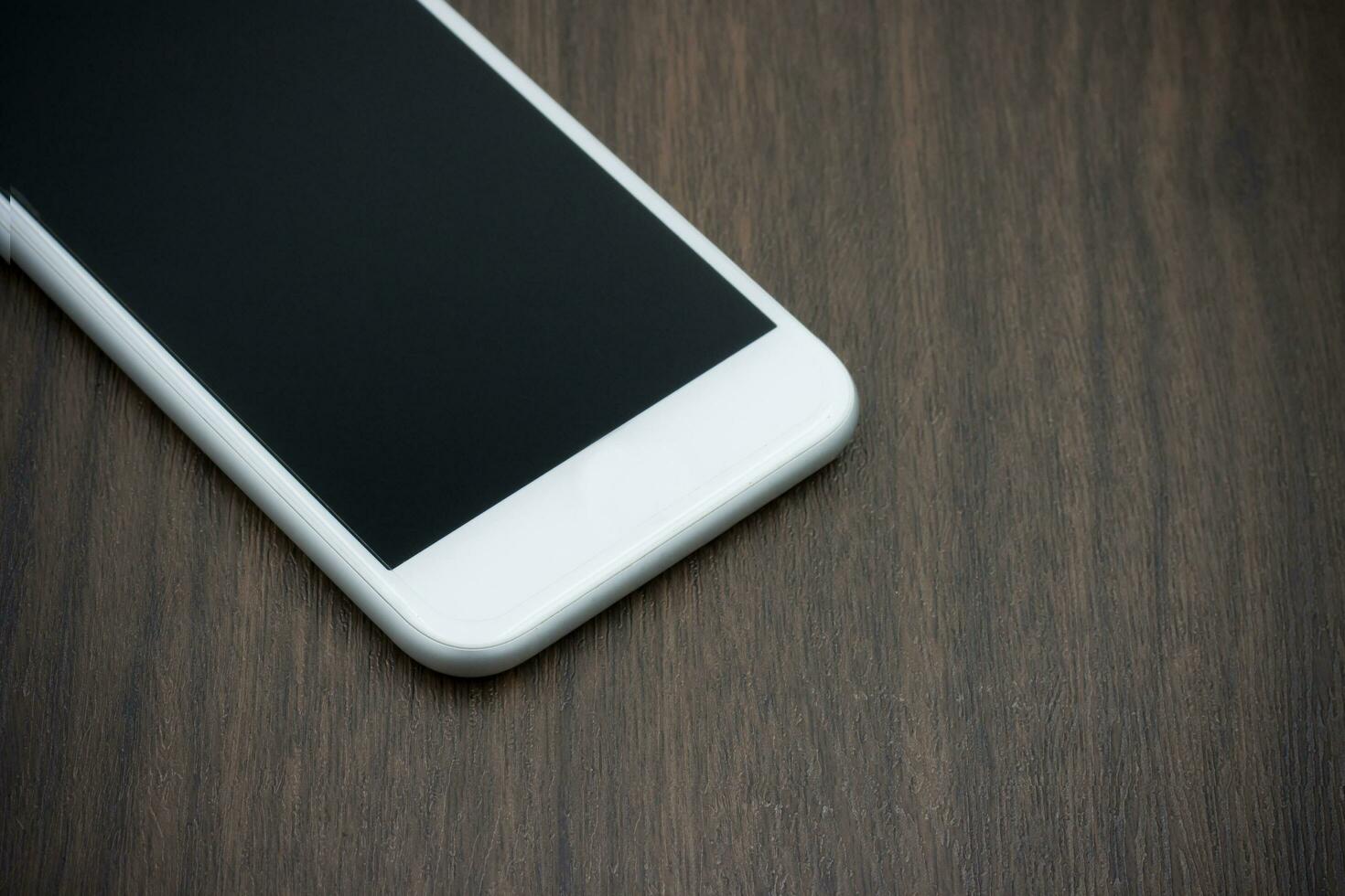 Smart phone in white color with blank screen on wooden table. photo