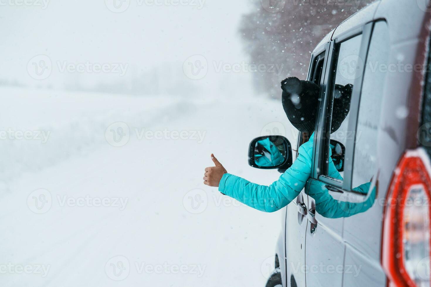 Happy Traveler driving car on snowy road and gesture finger up, woman Tourist enjoying snow forest view from the car window in winter season. Winter travel, Road trip, Exploring and Vacation concepts photo