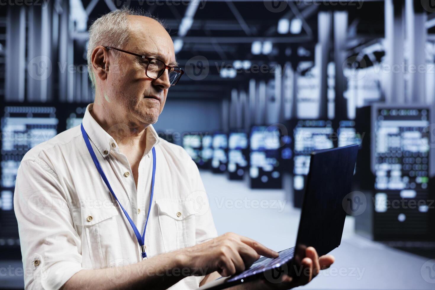 Senior IT developer inspects supercomputers in data center, ensuring smooth performance. Capable programmer in server farm monitoring energy consumption across units components using laptop photo