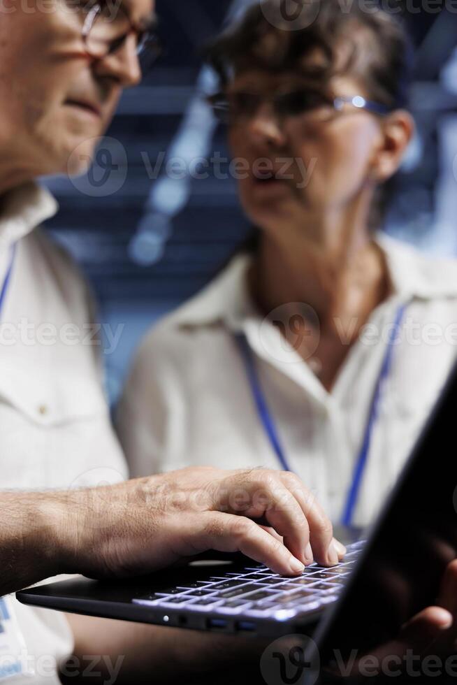 Octogenarian IT developers running analysis on server rows helping businesses manage databases, host websites and store files. Licensed programmers auditing high tech data center gadgets photo
