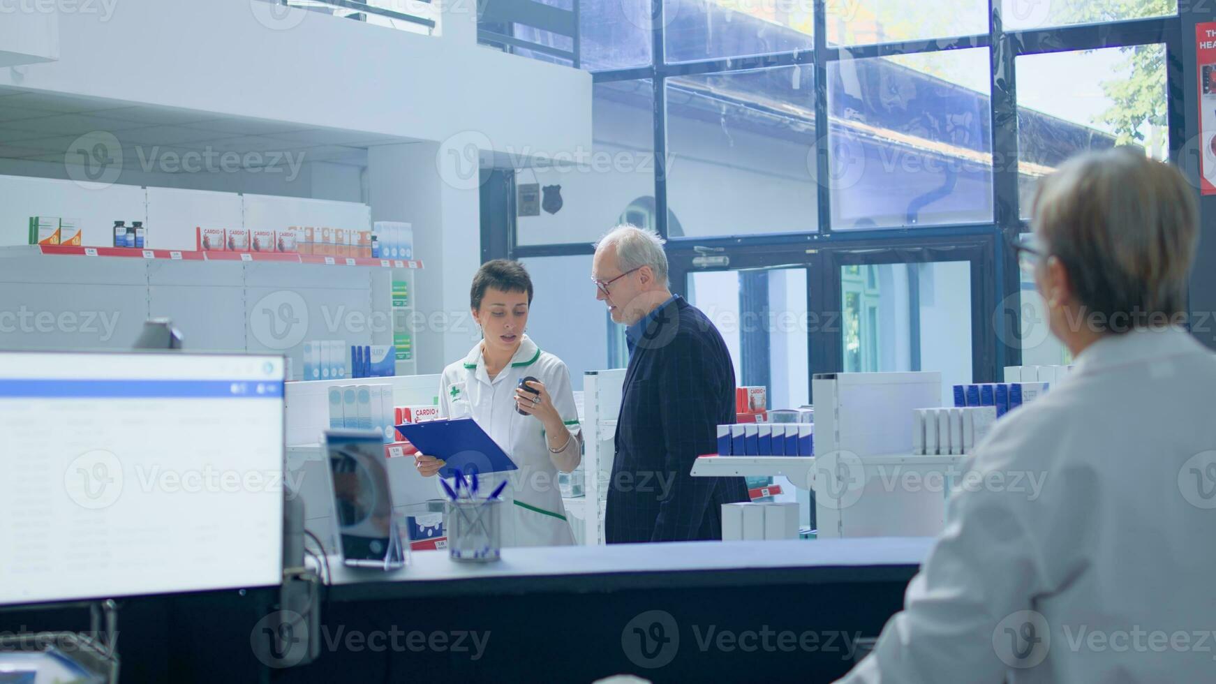 Elderly man in need of prescription medicaments informations in apothecary, requesting assistance from cashier who redirects him to qualified chemist checking pharmaceutical products inventory photo