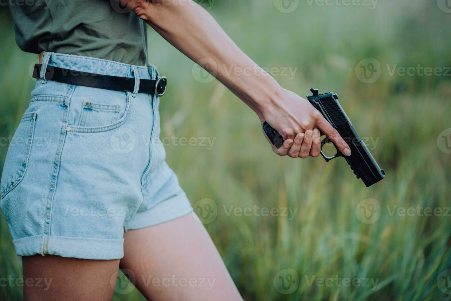 A girl in denim shorts and with a pistol in her hand poses for a photo.. Close-up photo