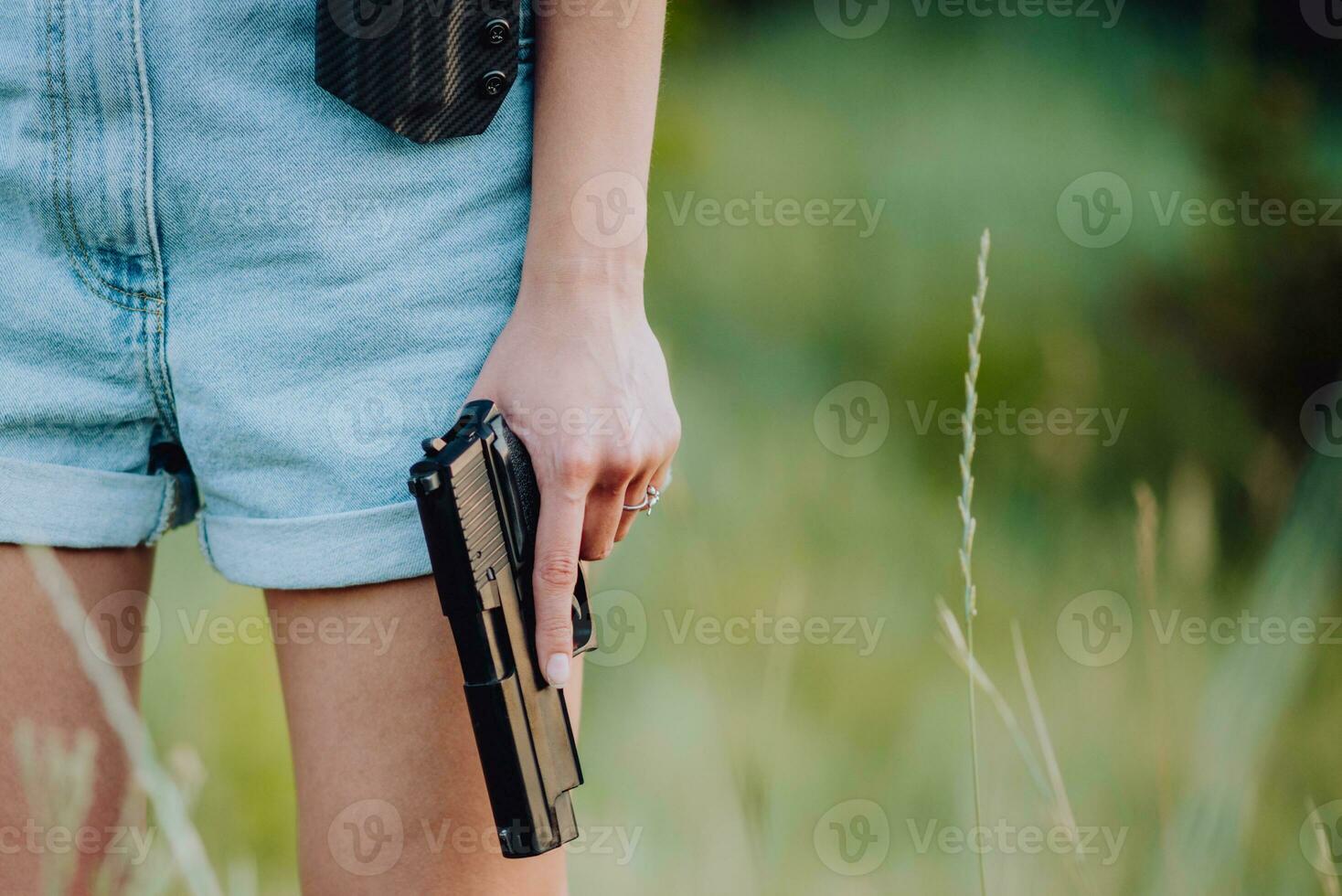 un niña en mezclilla pantalones cortos y con un pistola en su mano poses para un foto.. de cerca foto