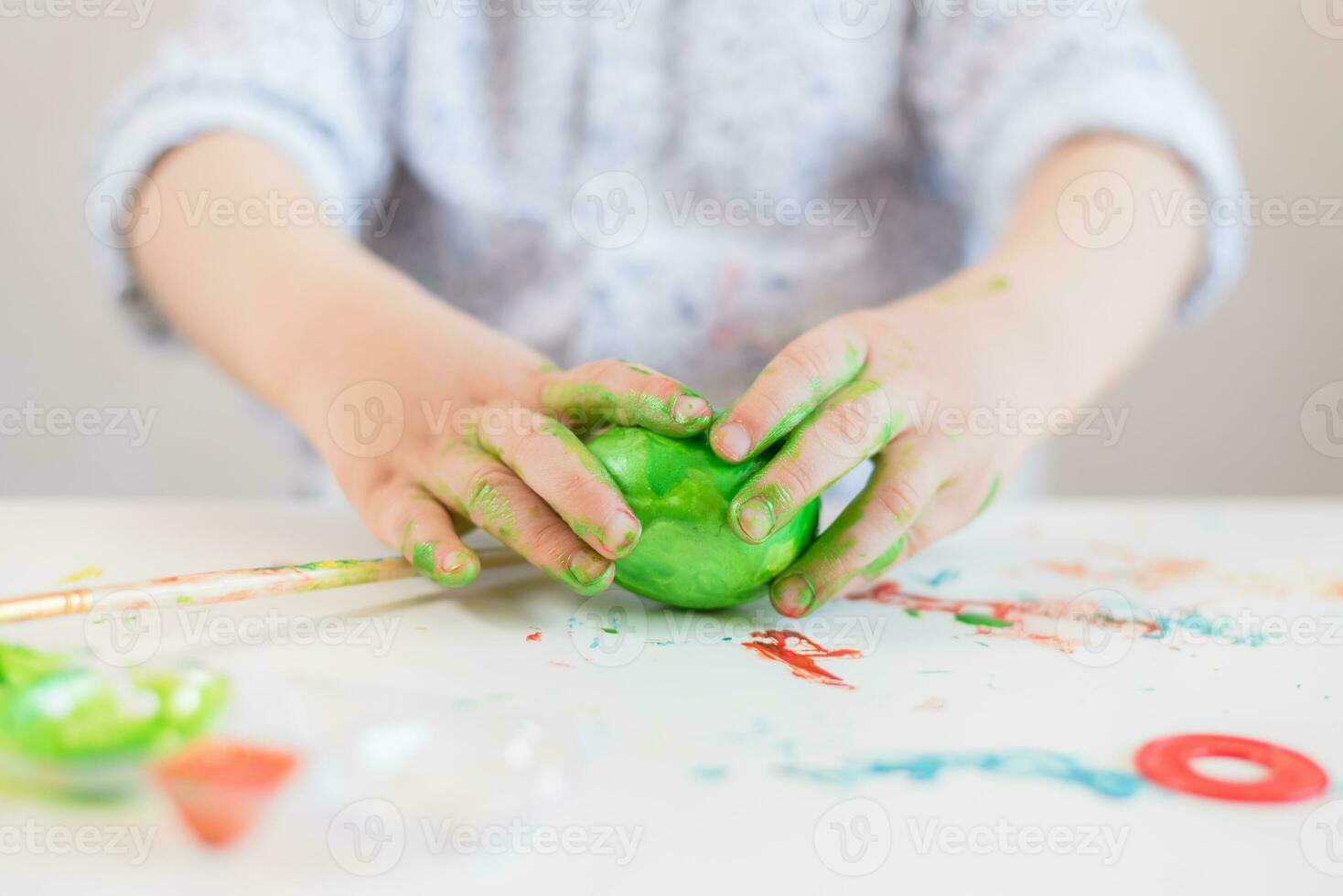 A child holds a green Easter egg in his hands stained with paint on a white table. photo