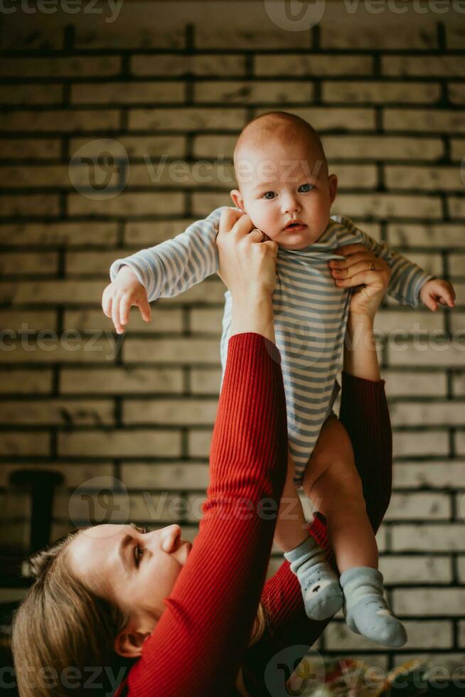 The mother lifts the baby above her head . The mom raise up in her hands child. A young woman has fun and rejoices with the infant. photo