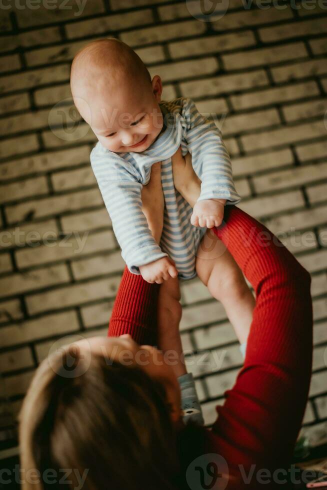 The mother lifts the baby above her head . The mom raise up in her hands child. A young woman has fun and rejoices with the infant. photo