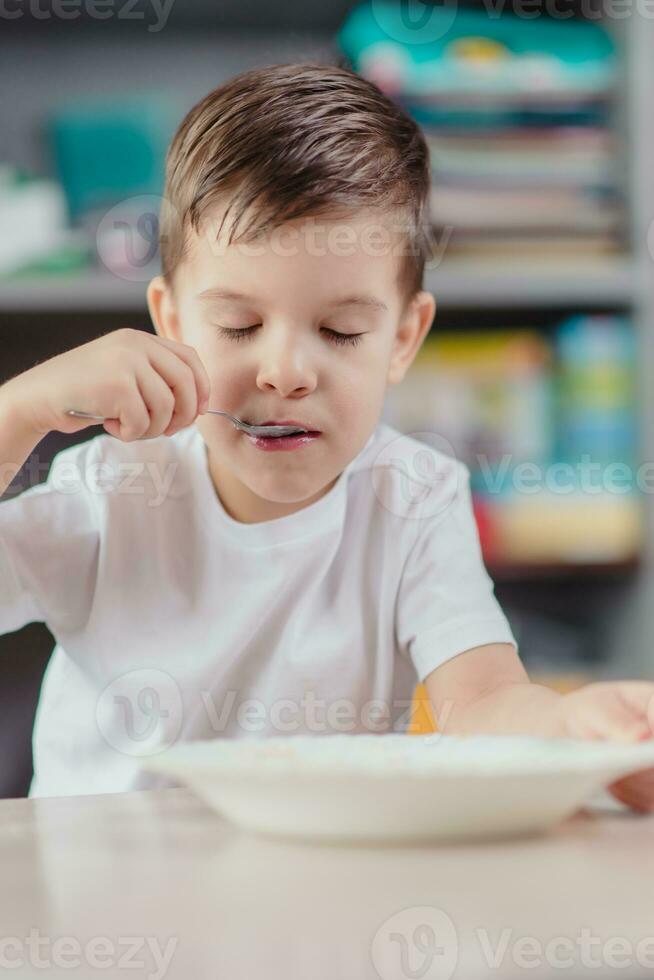 The child has breakfast with oatmeal porridge. The boy eats while sitting at a table in the kitchen at home. photo