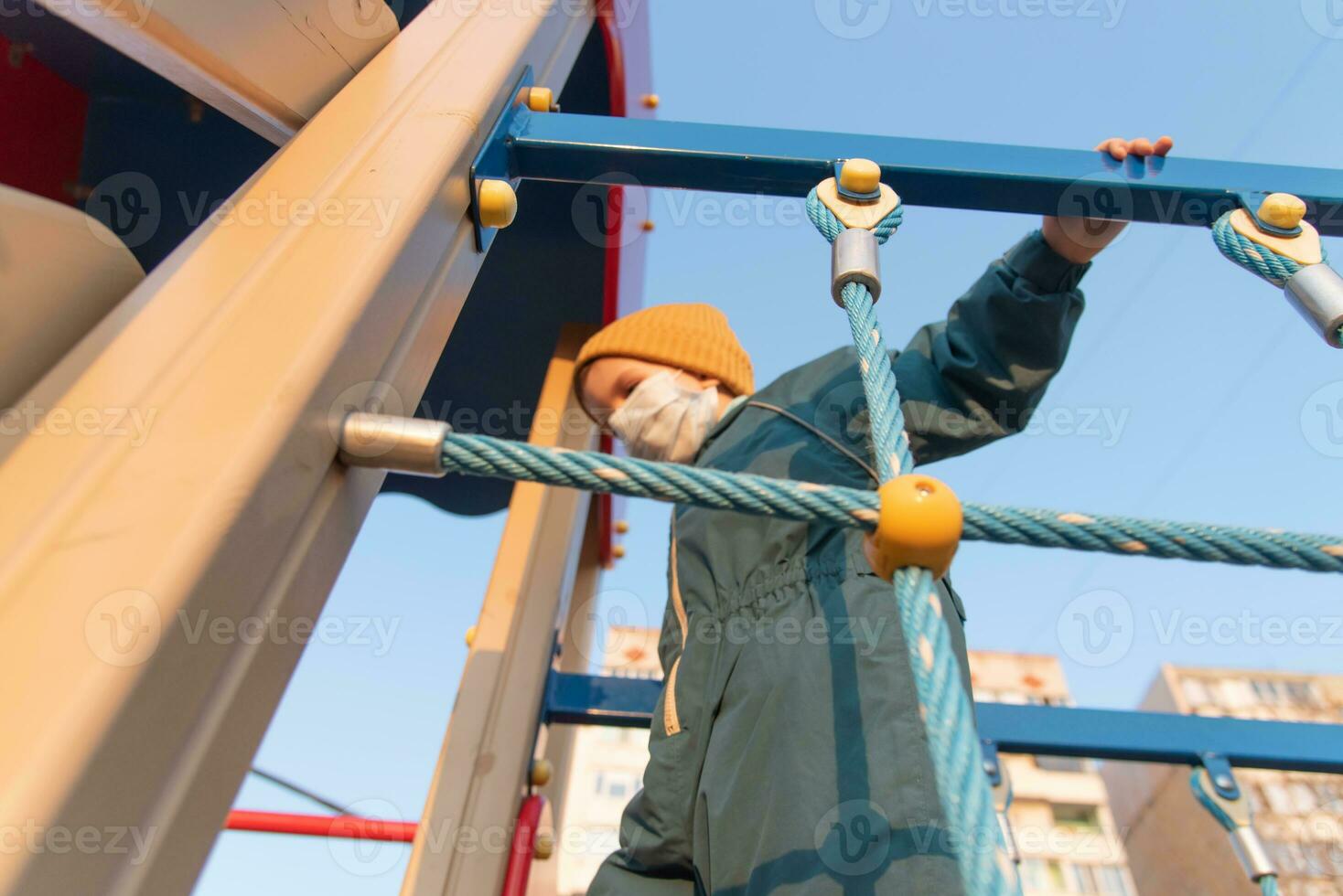 A child in a medical mask plays on the playground during the pandemic of coronavirus and Covid - 19 photo