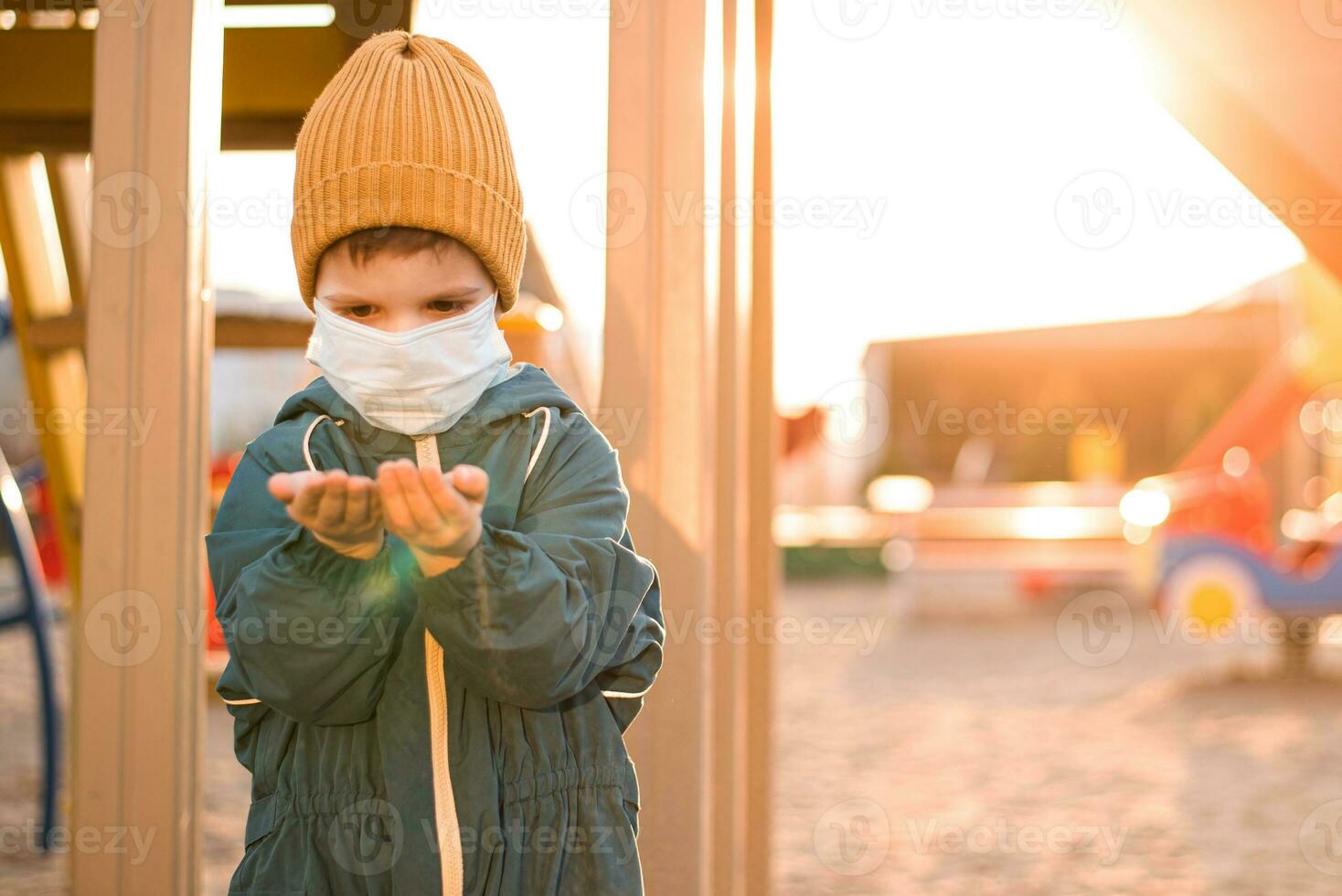 A boy in a protective mask plays in the playground and spills sand from his hands during the pandemic of coronavirus and Covid - 19 photo