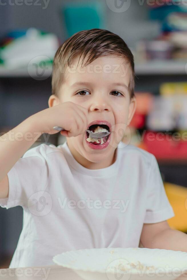 el niño tiene desayuno con harina de avena papilla. el chico come mientras sentado a un mesa en el cocina a hogar. foto