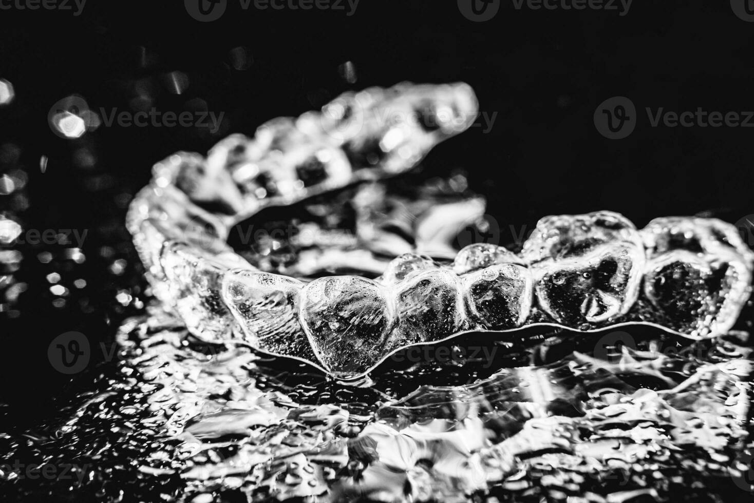 Transparent aligners, tooth retainers lie on a mirror with water droplets on a black background photo