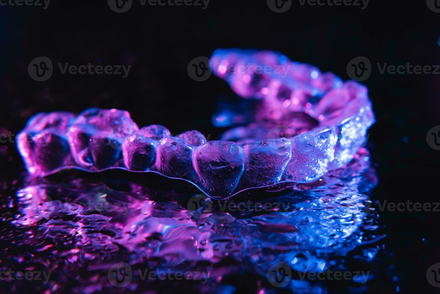 Transparent aligners, tooth retainers lie on a mirror with water droplets on a black background photo