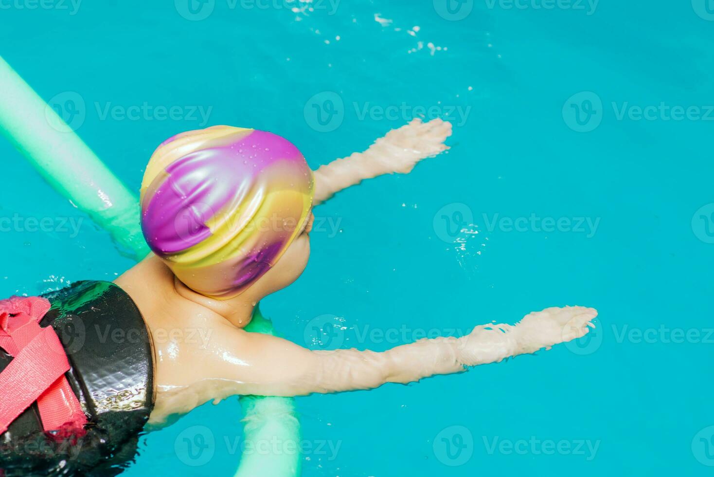 A little boy with a life jacket on his chest learns to swim in an indoor pool. photo