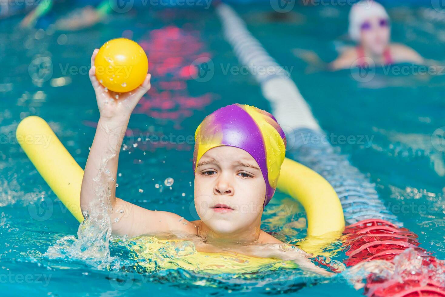 A little boy with a life jacket on his chest learns to swim in an indoor pool. photo