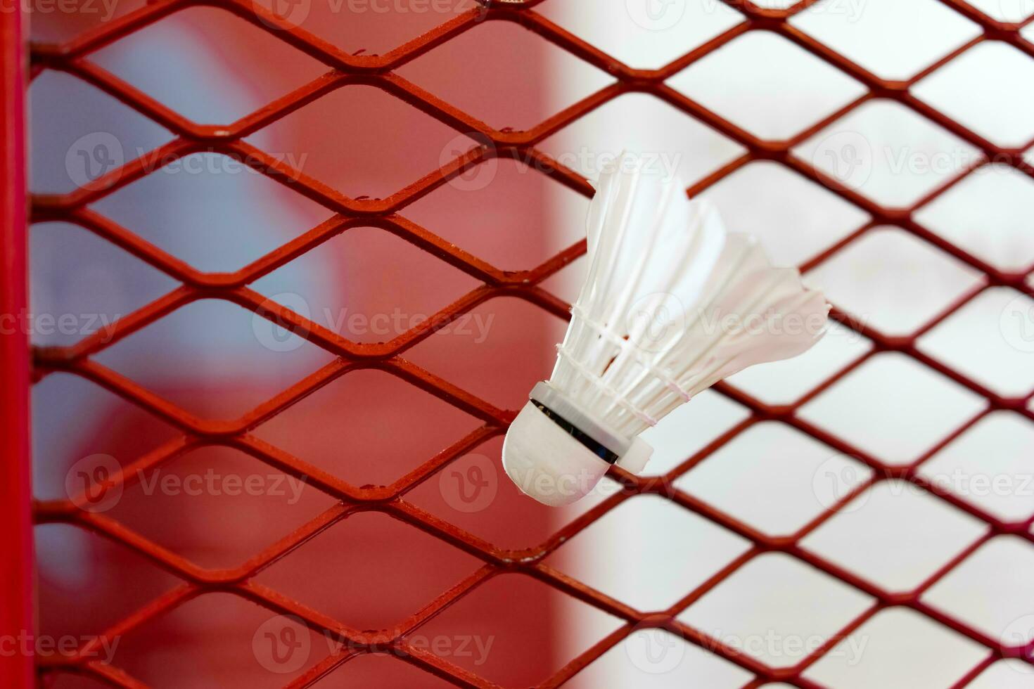 Shuttlecocks were stuck to the badminton steel grill net with a big red drawing of shuttlecock on background beside. photo