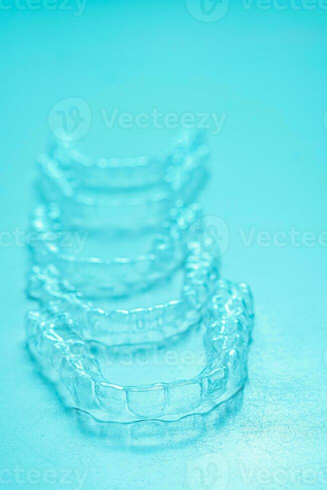 Invisible dental teeth brackets tooth aligners on turquoise background. Plastic braces dentistry retainers to straighten teeth. photo