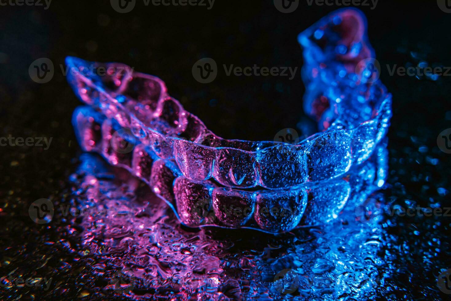 Transparent aligners, tooth retainers lie on a mirror with water droplets on a black background photo