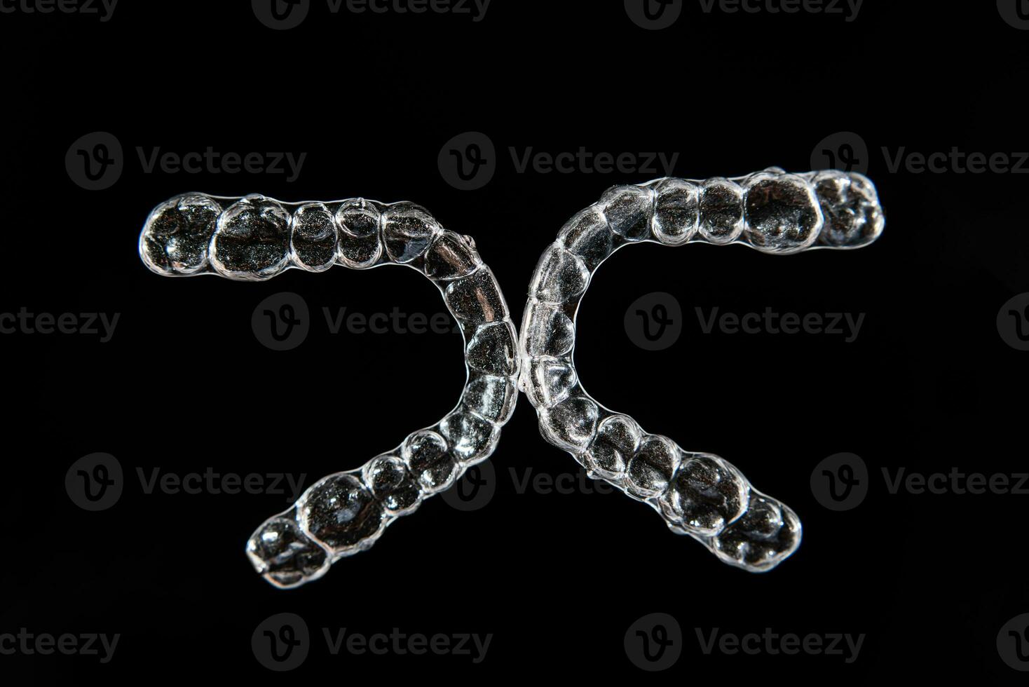 Invisible dental teeth brackets tooth aligners on black background. Plastic braces dentistry retainers to straighten teeth. photo