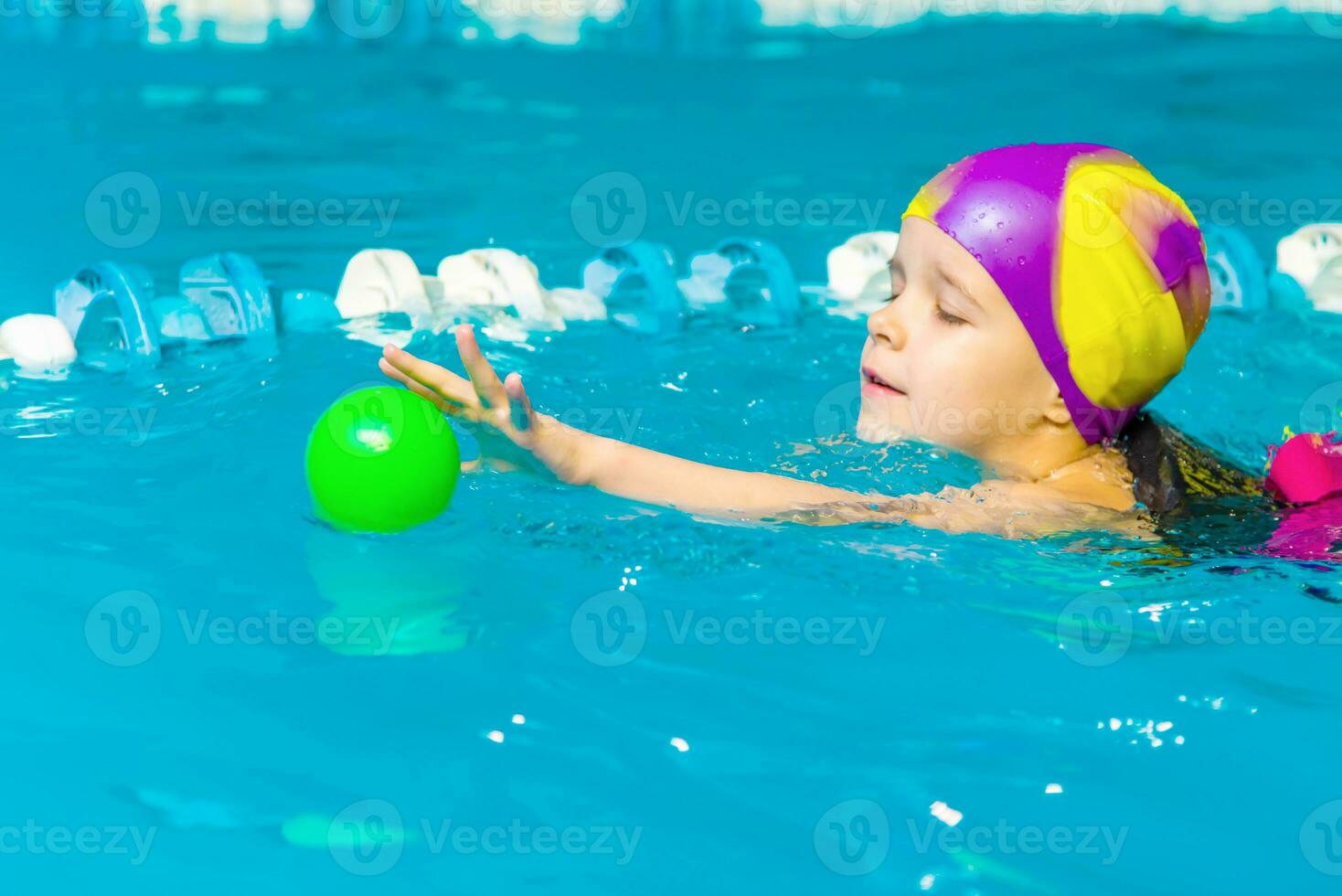 A little boy with a life jacket on his chest learns to swim in an indoor pool. photo