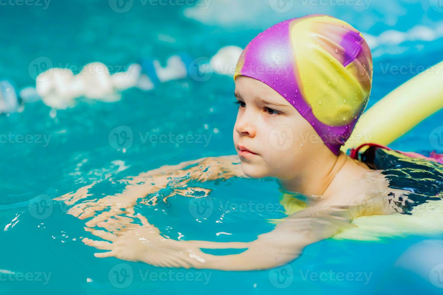 A little boy with a life jacket on his chest learns to swim in an indoor pool. photo