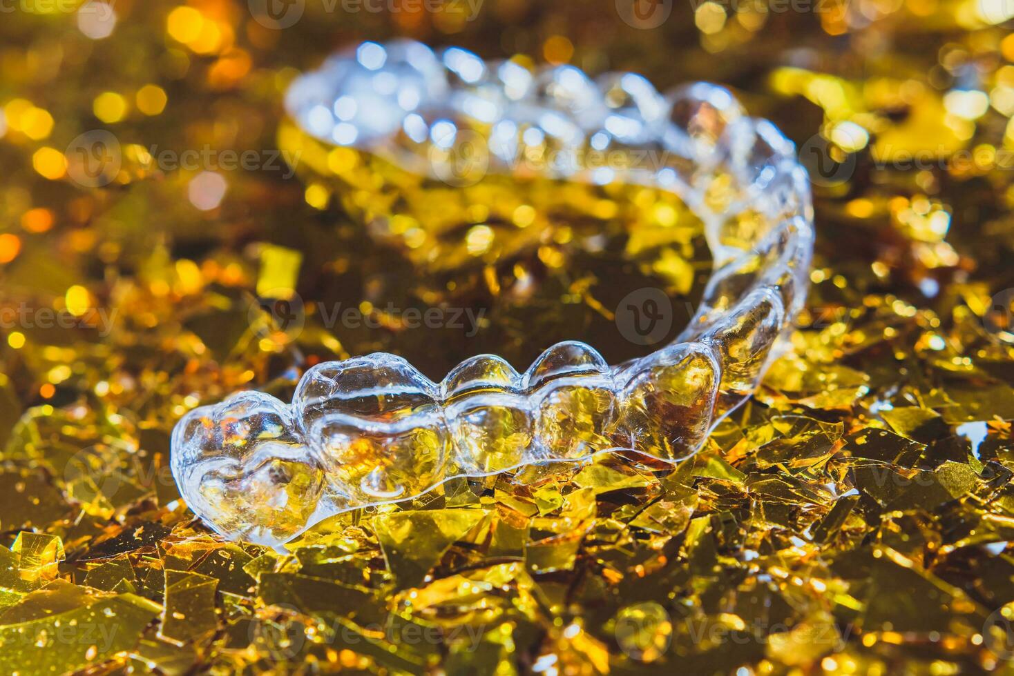 Invisible dental teeth brackets tooth aligners on gold background. Plastic braces dentistry retainers to straighten teeth. photo