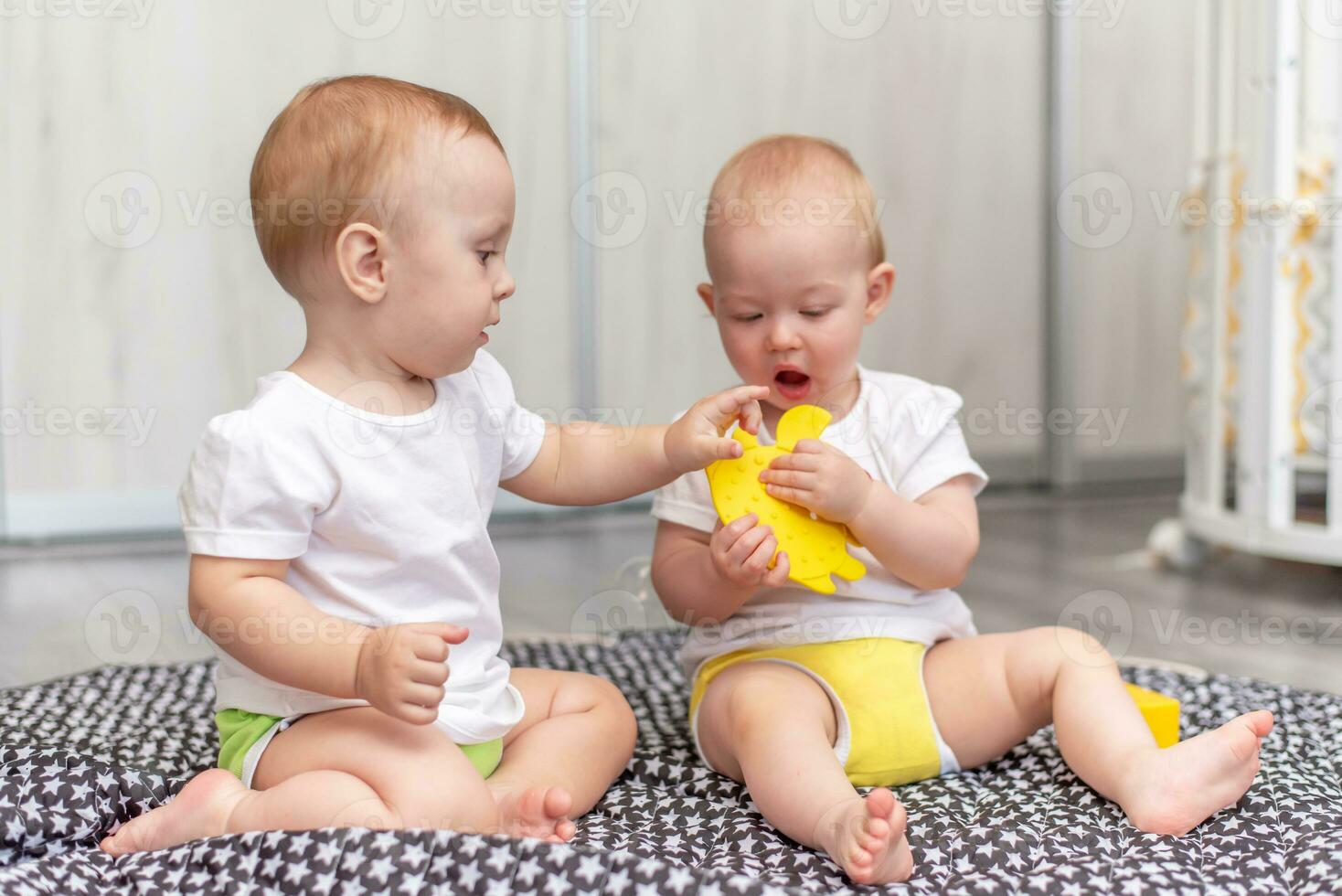 Cute happy kids play together on the floor with toys and take them into mouth photo