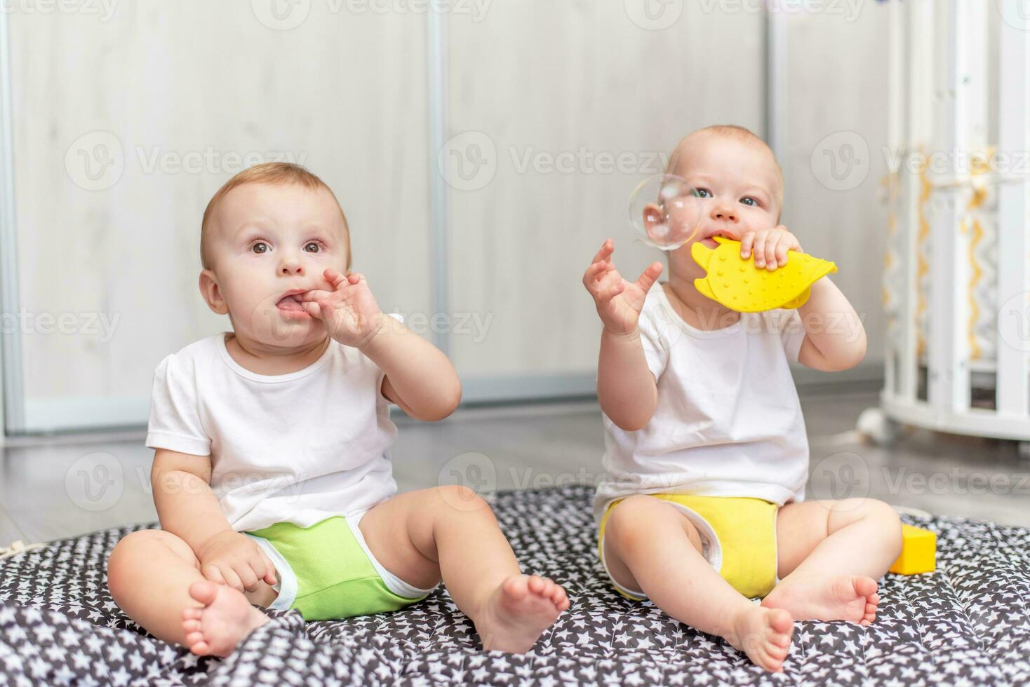 Cute happy kids play together on the floor with toys and take them into mouth photo