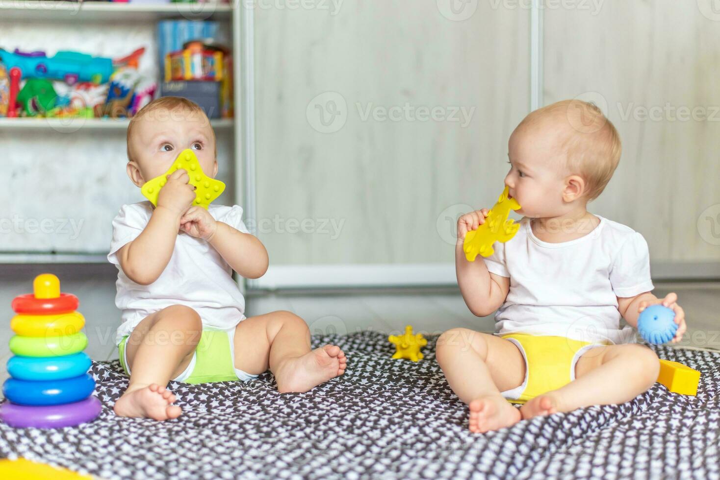 Cute happy babies play together on the floor with toys and take them in their mouths photo