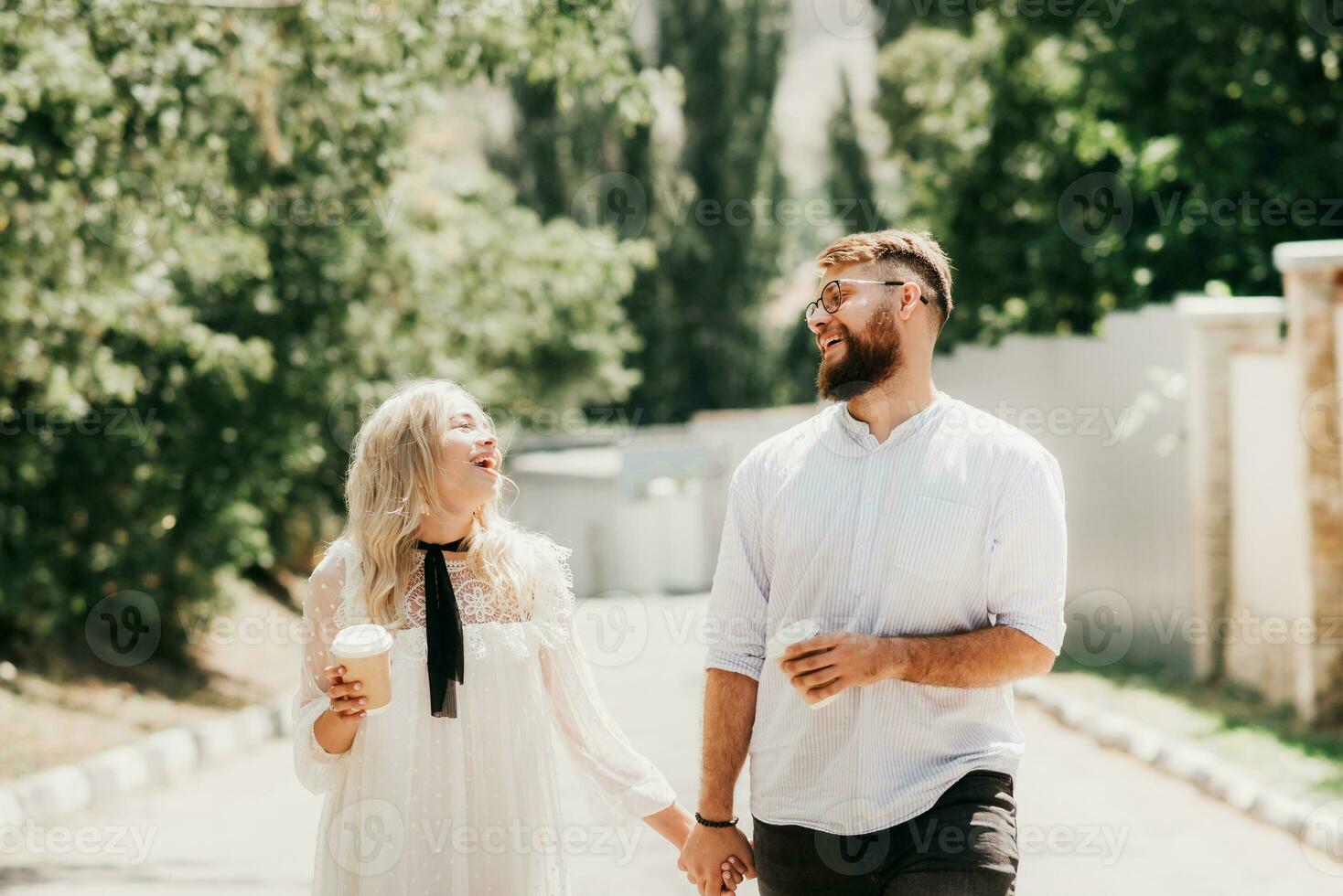 Laughing happy couple holding hands and drinking coffee outdoors in summer photo