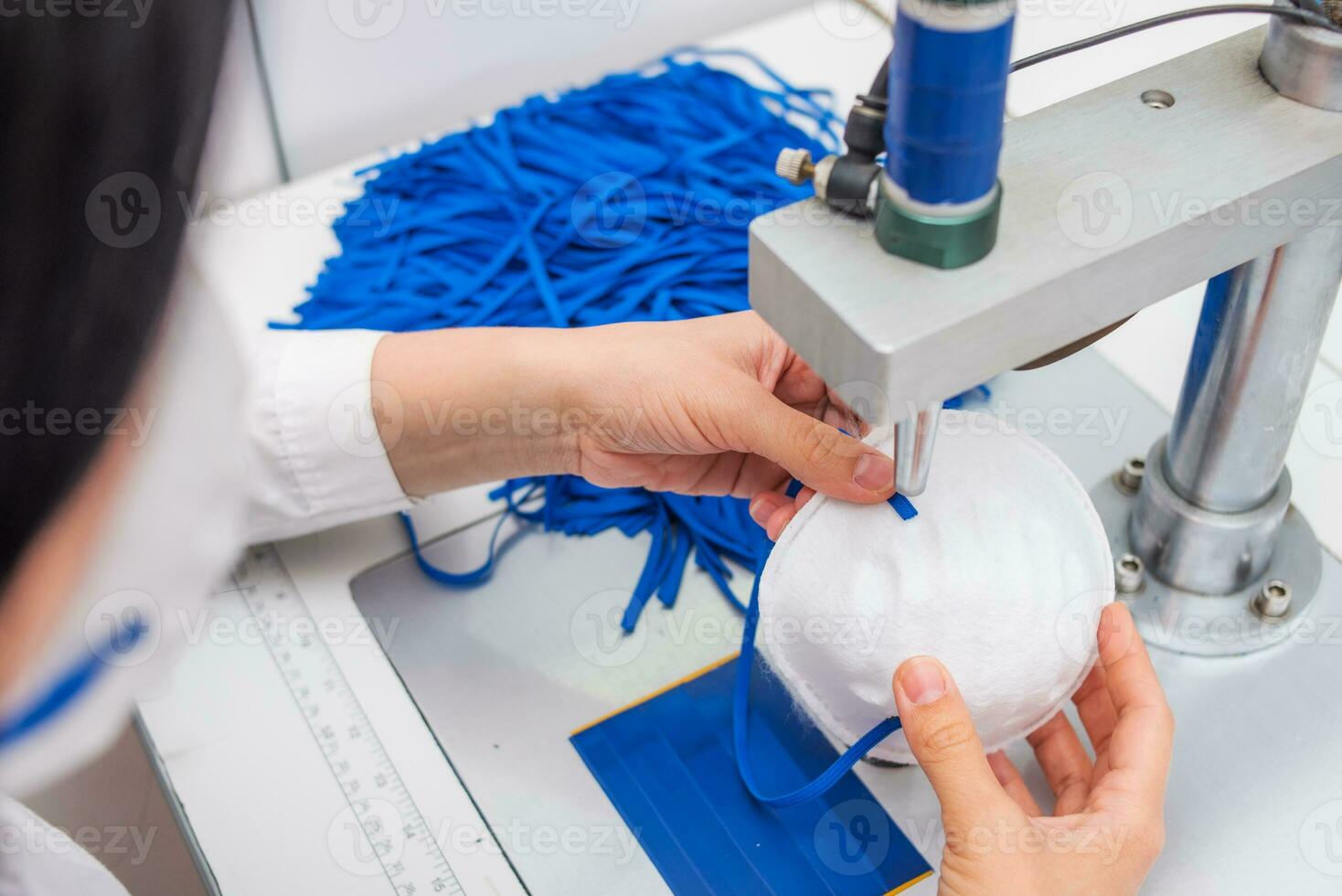 The girl works in a factory for the production of medical masks with nanofibre and solder loops with ultrasound on a machine. Coronavirus and Covid-19 Protection.Close-up. photo