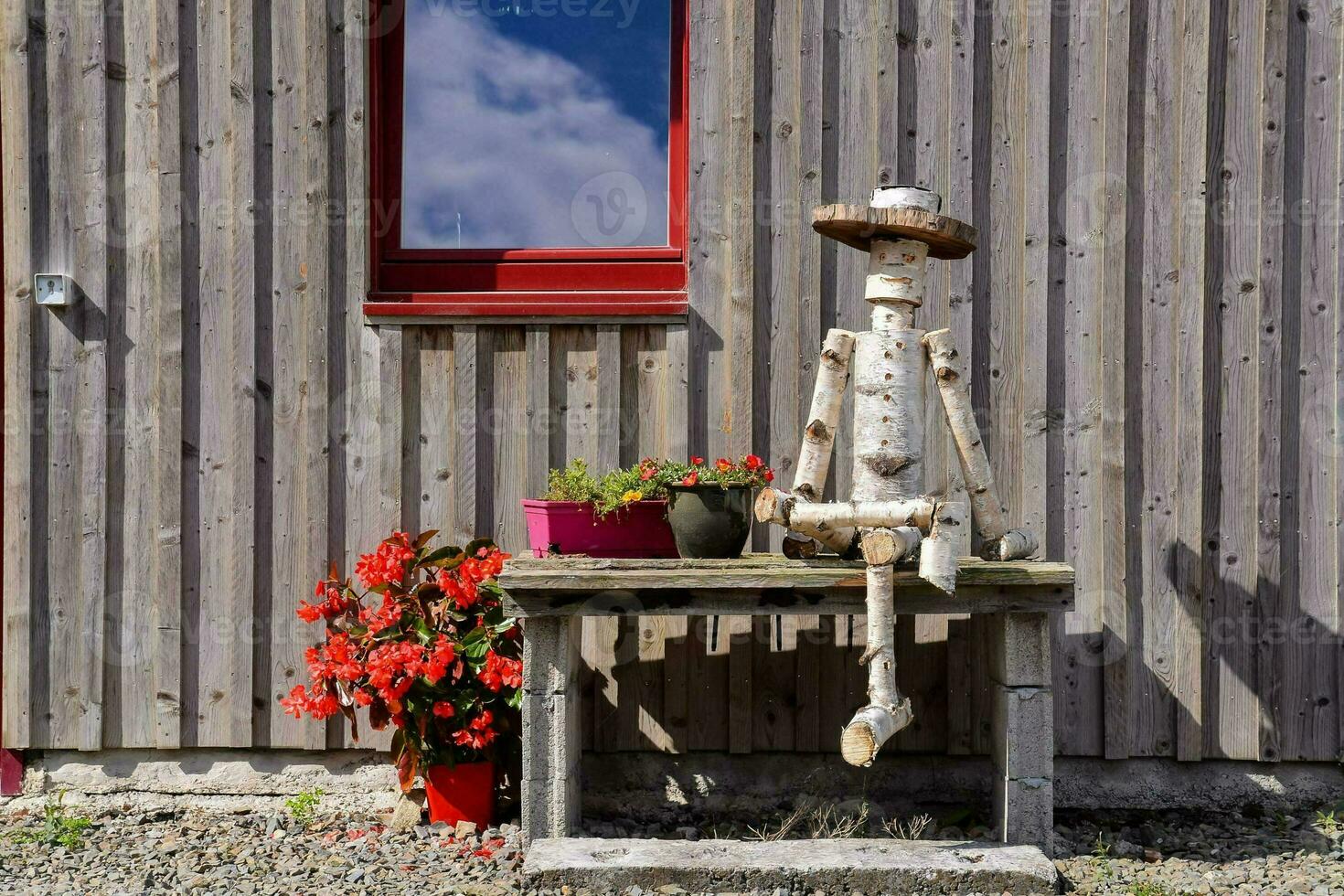 a wooden man sitting on a bench outside of a house photo