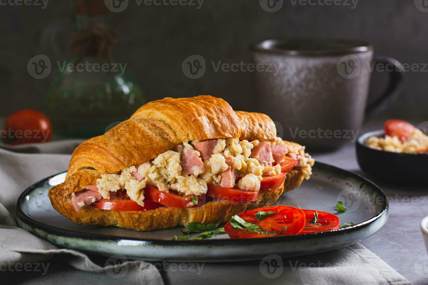 Appetizing croissant sandwich with scrambled eggs, sausages, tomatoes and herbs on a plate photo