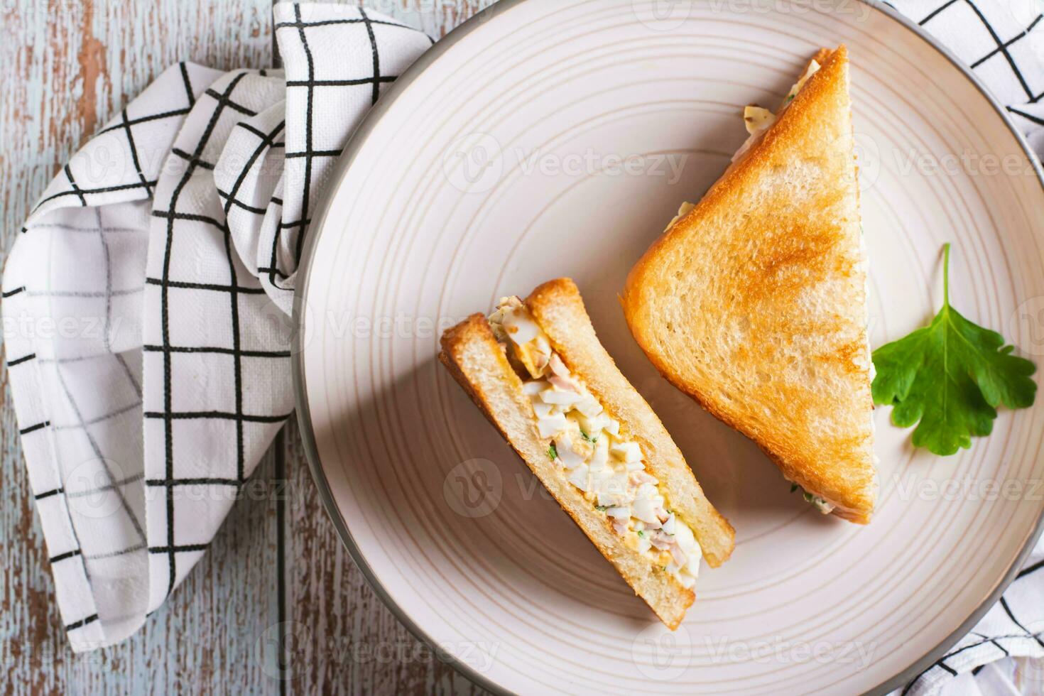 Close up of chopped sandwiches with egg, bacon and herbs salad on a plate on the table top view photo