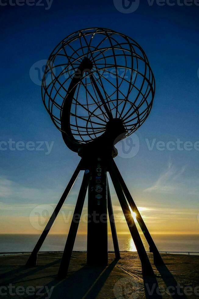 the sun sets behind a large globe in front of the ocean photo