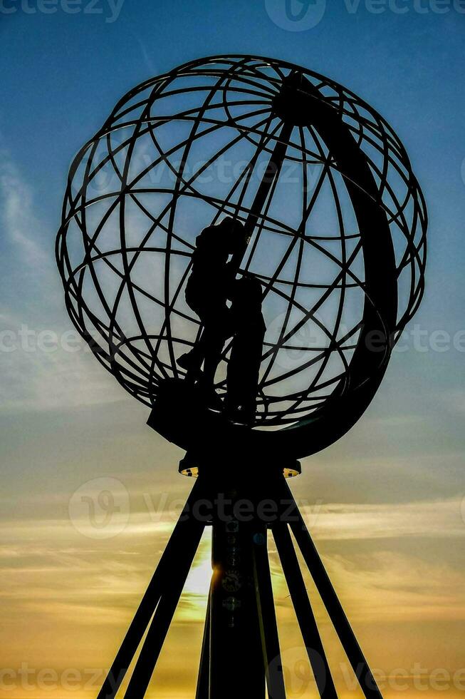 the sun sets behind a globe sculpture photo