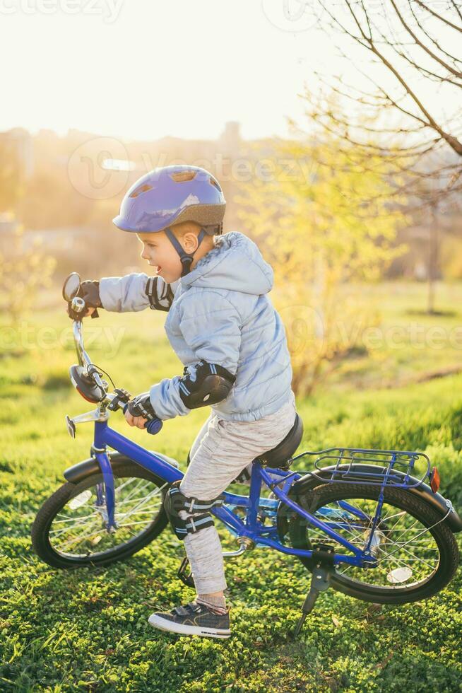 un niño en un casco aprende a paseo un bicicleta en un soleado día a puesta de sol foto