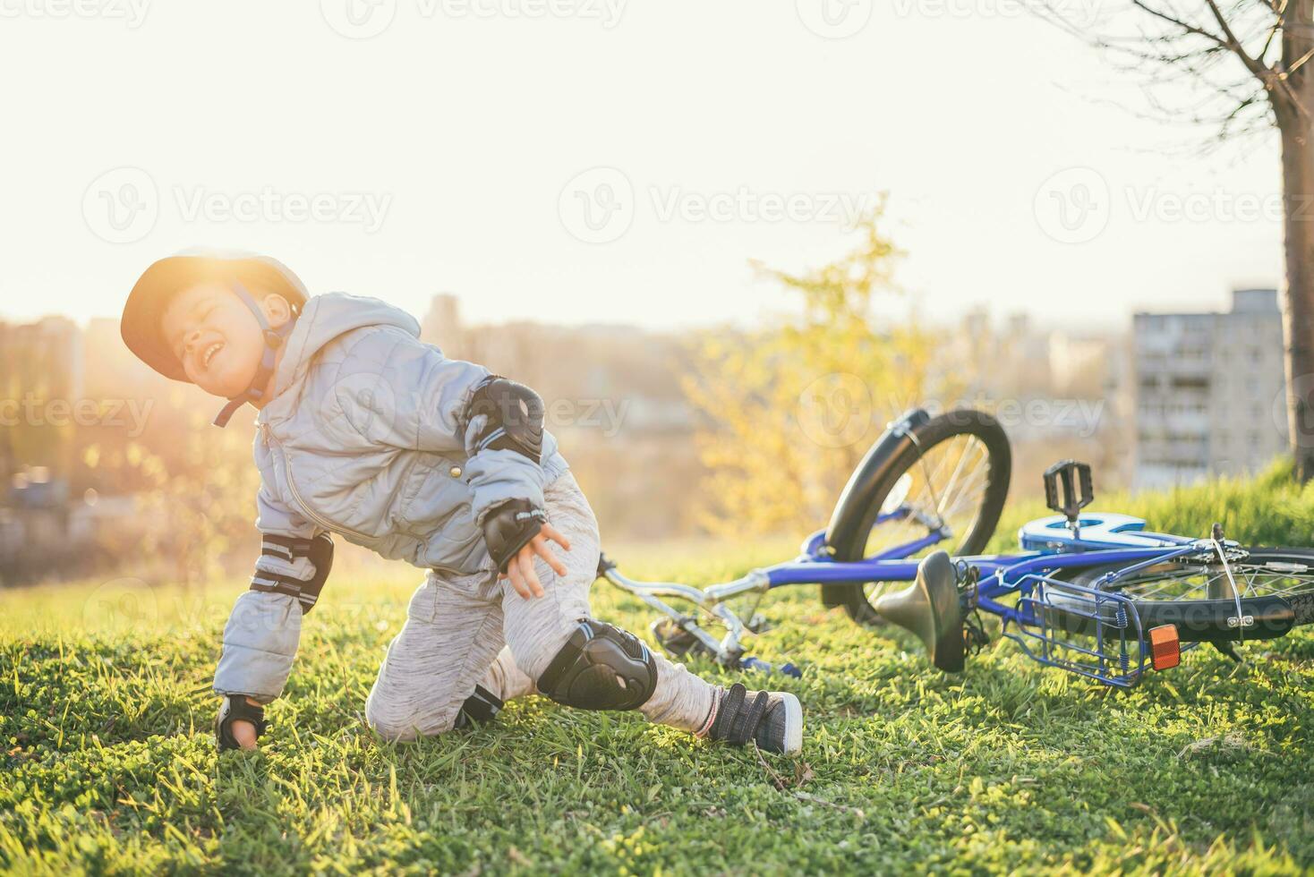 A small child in a helmet and protection fell from a bicycle onto the grass and was not injured photo