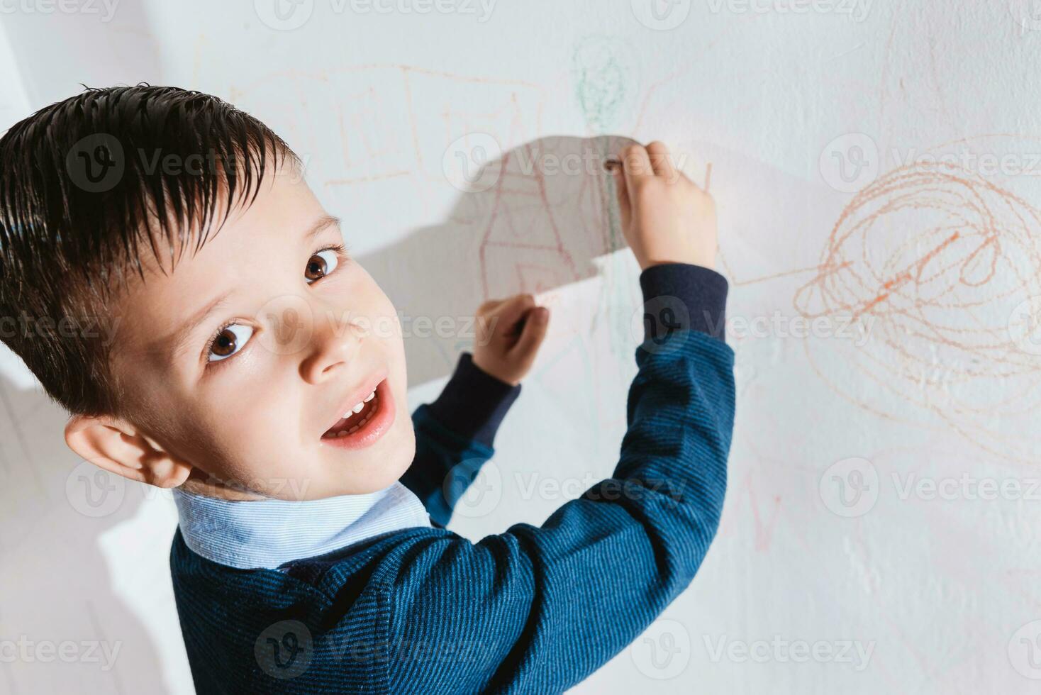 Cute child draws on the wall with colored crayons photo