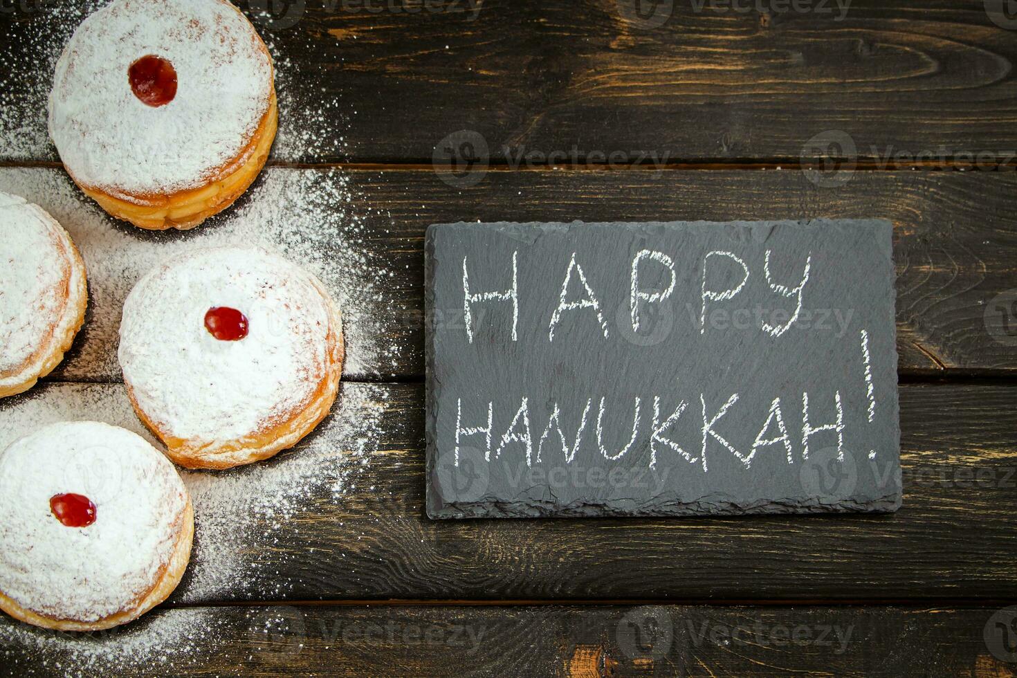 feliz Jánuca. postre tradicional sufganiyot sobre fondo de madera oscura. donuts, velas y regalos. celebrando la festividad judía. foto