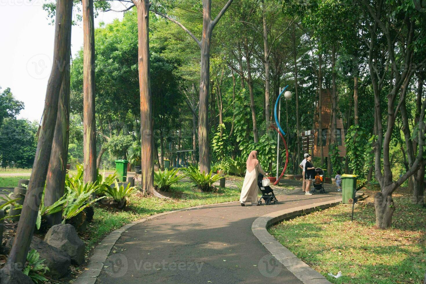 young hijab mother with little daughter with stroller walking together. Mom walks in the park with her daughter and holds her in her arms. view from the back photo