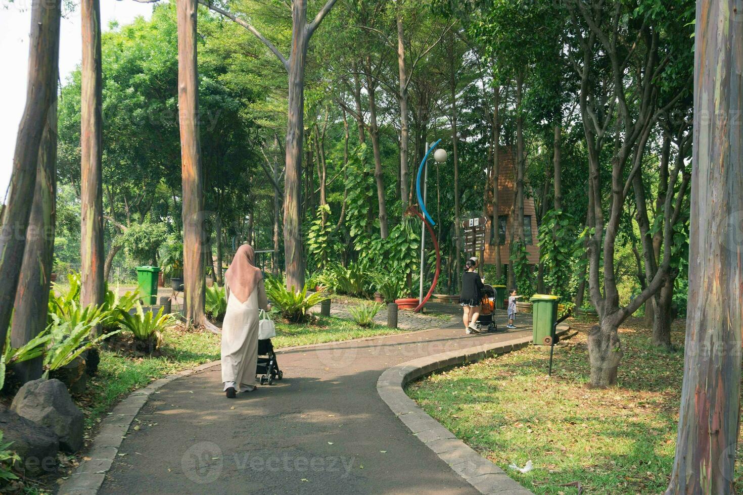 young hijab mother with little daughter with stroller walking together. Mom walks in the park with her daughter and holds her in her arms. view from the back photo