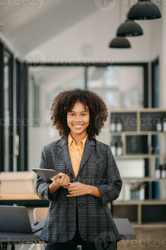 Confident business expert attractive smiling young woman typing laptop ang holding digital tablet  on desk in office. photo