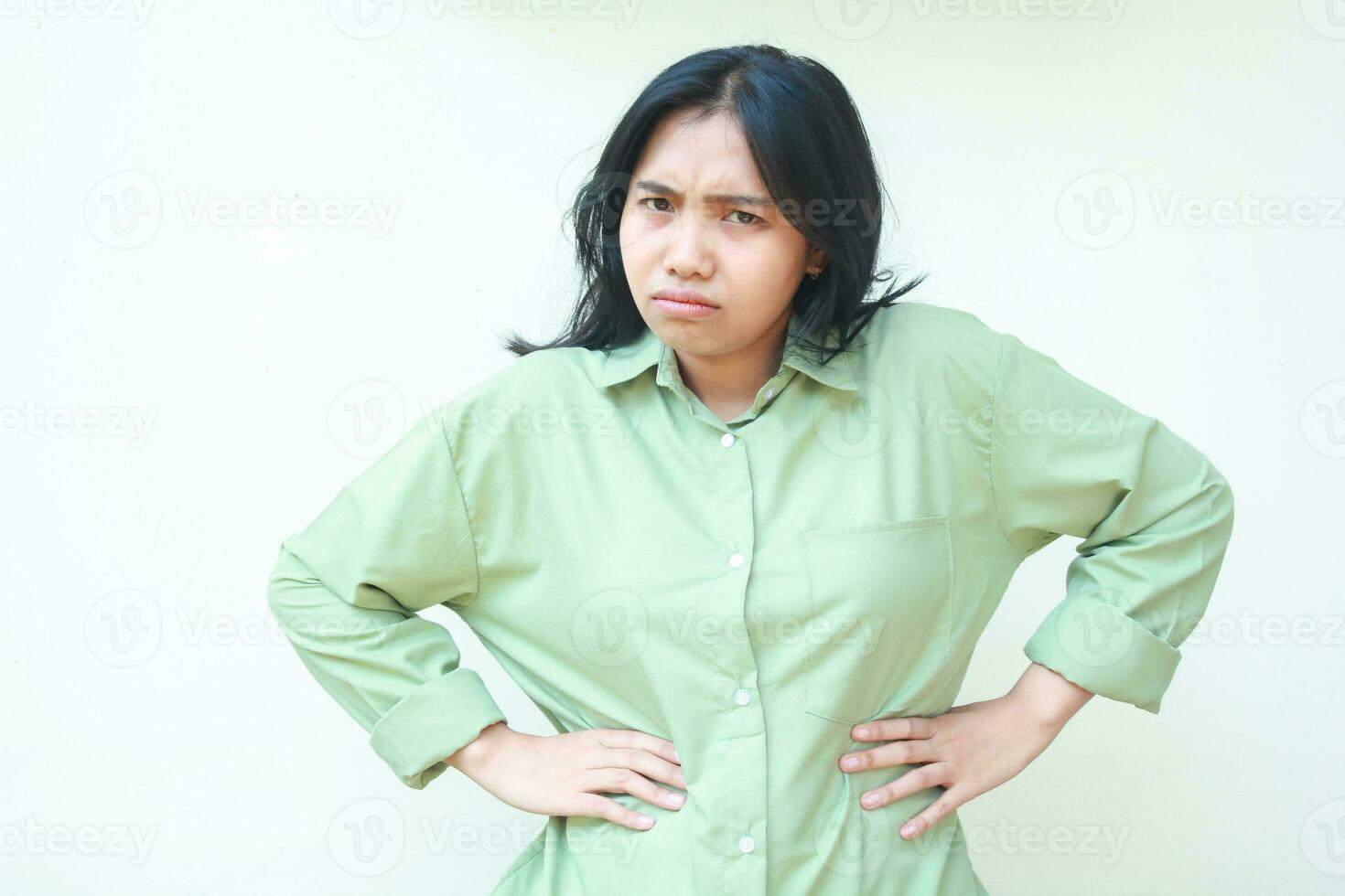 disgruntled asian woman looking at camera with hands on waist wearing green casual clothes show mad furious expression, isolated on white background photo
